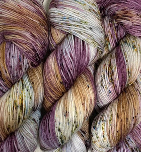 Speckled hand dyed yarn with sections of wine purple & gold. Speckles of grey, green, and purple throughout the skein.