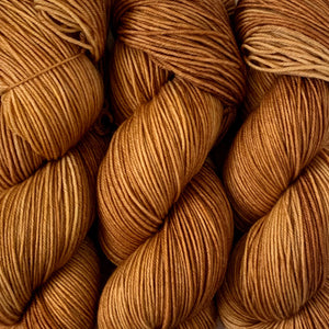 close up photo of 3 skeins of hand dyed wool yarn in a rich golden brown colour